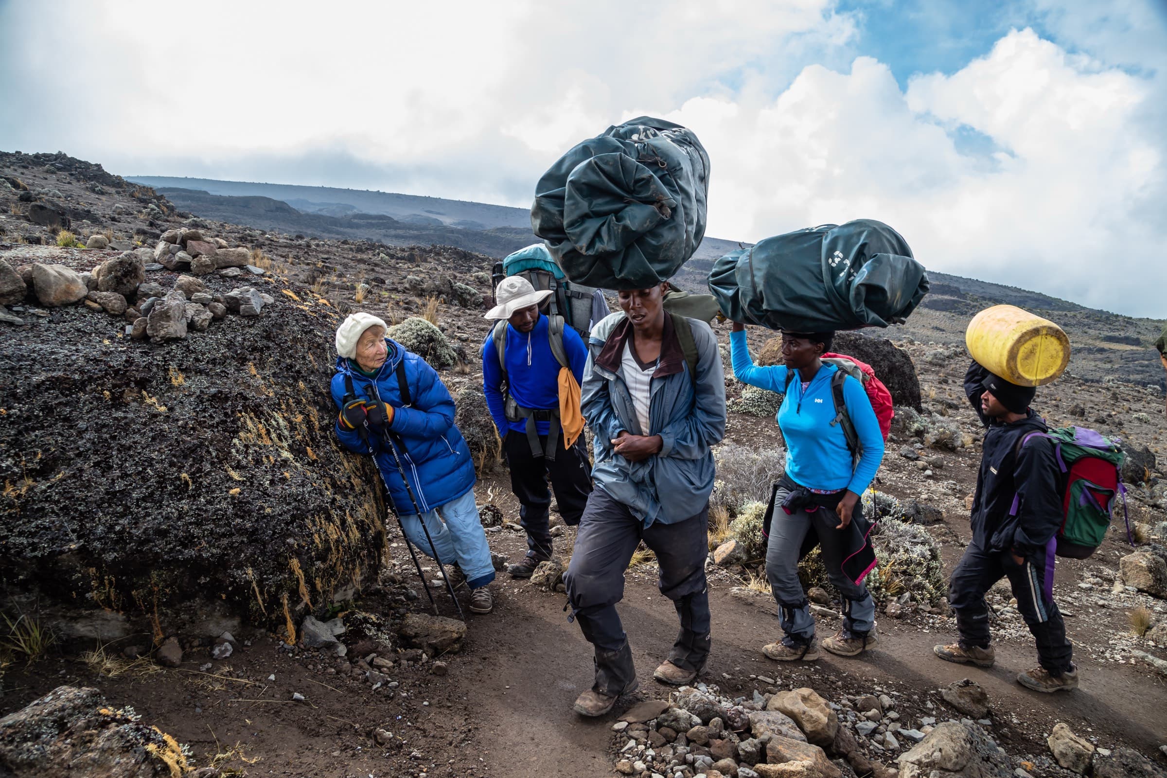 A line of porters carrying heavy duffel bags up a rocky trail